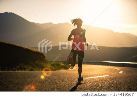 Woman runner running in sunset mountain road 134419507