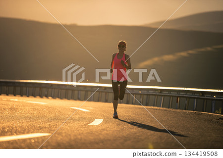 Woman runner running in sunset mountain road Woman runner running in sunset mountain road 134419508
