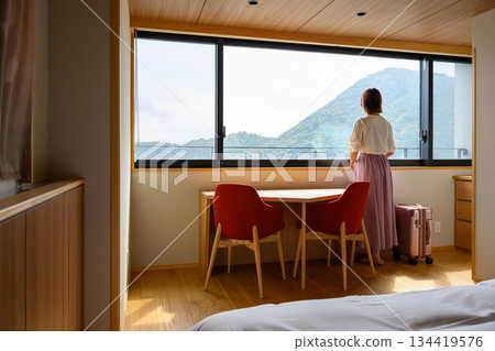 一位女士和她的行李箱靠在窗邊，眺望著遠方的山脈。 134419576