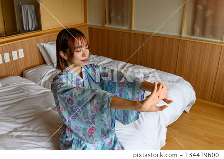 一名身穿浴衣的女子在床上伸展。 134419600