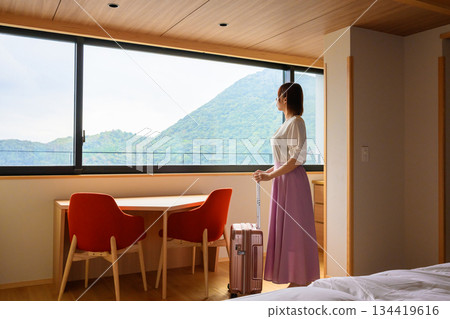 A woman in a hotel room looking out the window at the greenery A woman in a hotel room looking out the window at the greenery 134419616