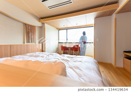 一位身穿浴衣的女子站在飯店房間的窗邊。 一位身穿浴衣的女子站在飯店房間的窗邊。 134419634