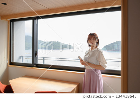 A woman in her twenties holding a smartphone by the window 134419645