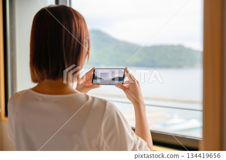 一位女士正用智慧型手機拍攝窗外的風景。 一位女士正用智慧型手機拍攝窗外的風景。 134419656