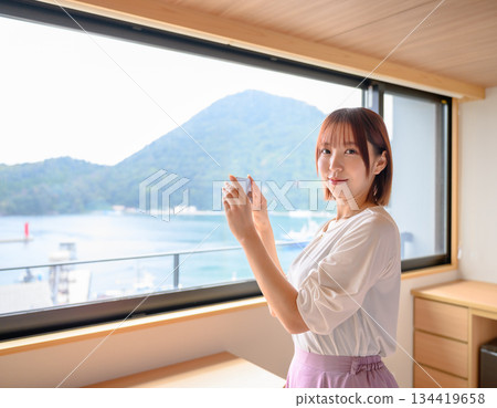 A woman taking a photo of the view outside her hotel room 134419658