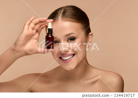 Beauty woman holds serum in studio for skincare routine focusing on glow and health of the skin with natural light 134419717