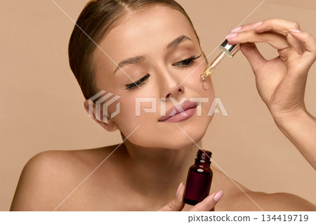Close-up of young woman applying face serum. woman with dropper and facial skincare cosmetics for beauty, hydration or oil treatment for healthy face. Close-up of young woman applying face serum. woman with dropper and facial skincare cosmetics for beauty, hydration or oil treatment for healthy face. 134419719