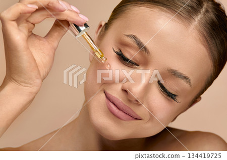 Portrait, beauty woman with serum, skincare and facial treatment for healthy skin or glow. Studio background, oil and person with cosmetics for shine, anti aging and wellness for face 134419725