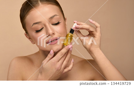 Beauty woman holds serum in a studio, demonstrating skincare routine for healthy skin and glow with focus on facial treatment and wellness 134419729