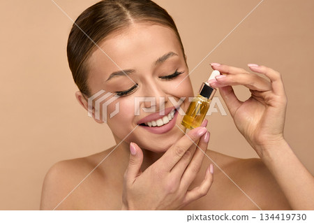 Beauty woman holds serum for skincare in studio, focusing on facial treatment for healthy skin in wellness routine Beauty woman holds serum for skincare in studio, focusing on facial treatment for healthy skin in wellness routine 134419730