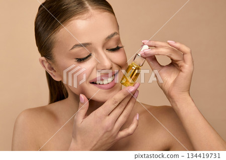 Beauty woman holds serum in studio and smiles while applying skincare for glowing and healthy skin 134419731
