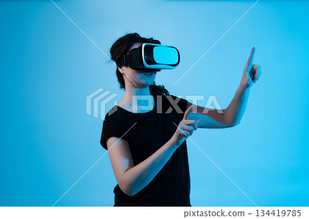 Woman interacting with virtual environment using VR headset and multi-directional gestures on blue background 134419785
