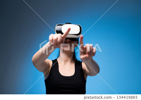 Young woman using VR headset with extended hands interacting with virtual controls in bright blue environment Young woman using VR headset with extended hands interacting with virtual controls in bright blue environment 134419865