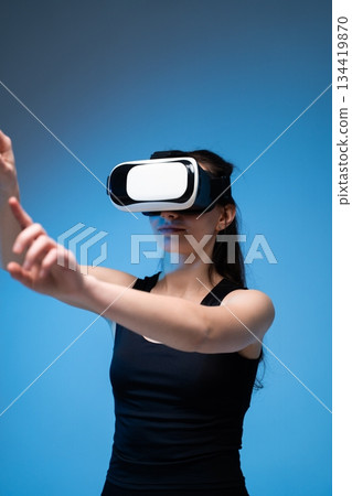 A woman in a VR headset uses both arms to interact with virtual elements, demonstrating immersive technology A woman in a VR headset uses both arms to interact with virtual elements, demonstrating immersive technology 134419870