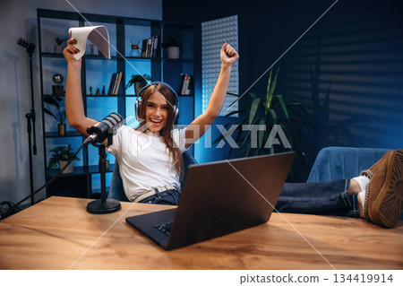 Celebrating, with hands up. Woman is hosting radio podcast with microphone and laptop 134419914