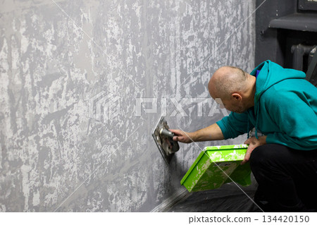 Focused worker applies decorative plaster to an interior wall using a trowel 134420150