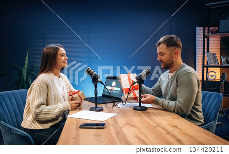 Woman is holding Christmas gift box. Radio hosts recording podcast 134420211