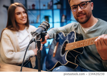 With acoustic guitar. Male musician on the radio podcast with female host With acoustic guitar. Male musician on the radio podcast with female host 134420230