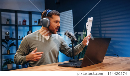By the laptop. Man with microphone in the studio, conception of podcast By the laptop. Man with microphone in the studio, conception of podcast 134420274