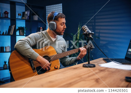 In headphones, playing guitar. Man with microphone in the studio, conception of podcast In headphones, playing guitar. Man with microphone in the studio, conception of podcast 134420301