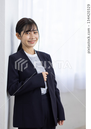 一位身穿西裝的年輕女子在窗邊微笑 134420329