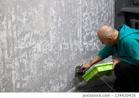 Man skillfully applies decorative plaster to a wall, enhancing the interior of an apartment Man skillfully applies decorative plaster to a wall, enhancing the interior of an apartment 134420416