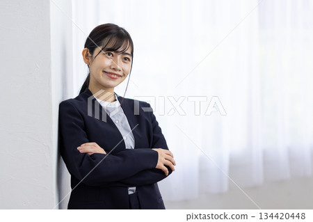A young woman in a suit smiling with her arms crossed by the window A young woman in a suit smiling with her arms crossed by the window 134420448