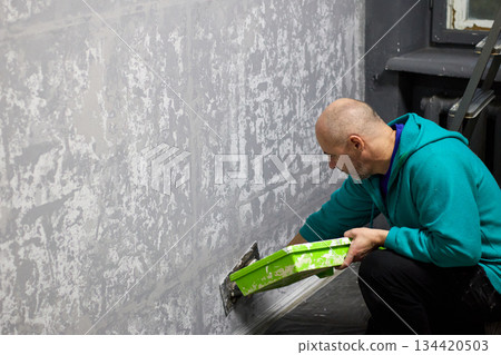 A skilled plasterer masterfully applies decorative plaster to a wall with a trowel 134420503
