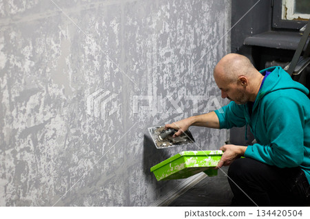 Man skillfully applies decorative plaster to a wall using a trowel Man skillfully applies decorative plaster to a wall using a trowel 134420504