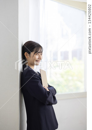 A young businesswoman in a suit smiling by the window while holding a binder 134420802
