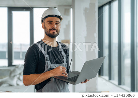 Silver colored laptop in hands. A man is renovating an unfinished room Silver colored laptop in hands. A man is renovating an unfinished room 134420866