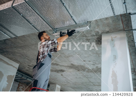 Installing the ceiling. A man is renovating an unfinished room Installing the ceiling. A man is renovating an unfinished room 134420928
