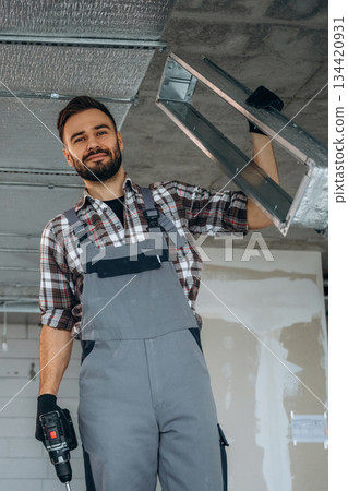 Installing the ceiling. A man is renovating an unfinished room Installing the ceiling. A man is renovating an unfinished room 134420931