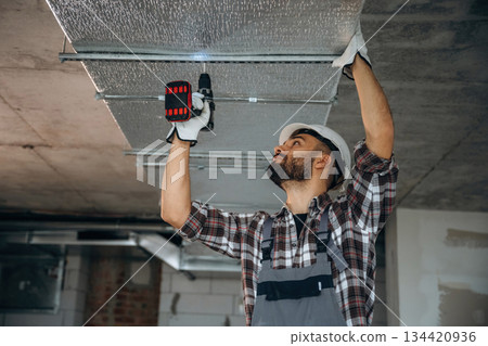 Ceiling work, using a drill. A man is renovating an unfinished room Ceiling work, using a drill. A man is renovating an unfinished room 134420936