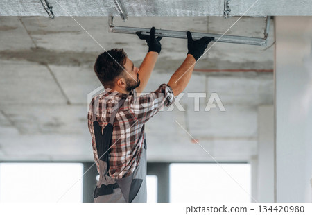 In gloves, ceiling work. A man is renovating an unfinished room In gloves, ceiling work. A man is renovating an unfinished room 134420980
