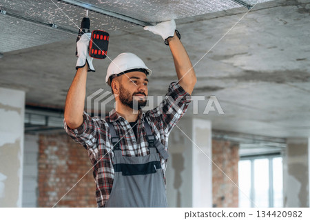 In gloves, ceiling work. A man is renovating an unfinished room 134420982