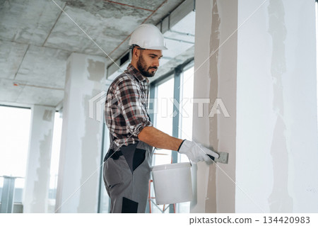 Puttying the wall. A man is renovating an unfinished room 134420983