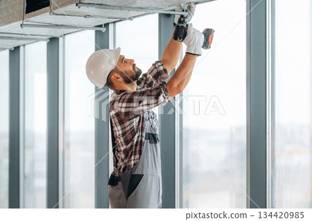 Hands are up, ceiling work. A man is renovating an unfinished room 134420985