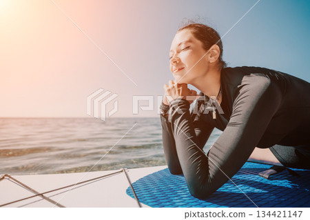Woman, Surfboard, Ocean - Young woman relaxing on surfboard at the beach at sunset. Woman, Surfboard, Ocean - Young woman relaxing on surfboard at the beach at sunset. 134421147