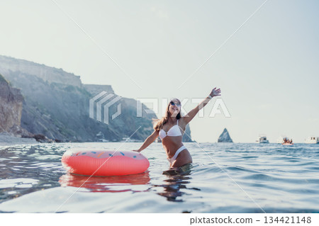 Woman, swimming, ocean. Happy young woman enjoying summer vacation with inflatable donut in clear blue sea near cliffs. 134421148