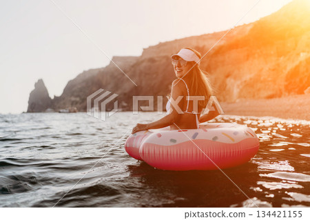 Woman, ocean, donut float, happy woman enjoying summer vacation in clear sea near cliffs with copy space. 134421155