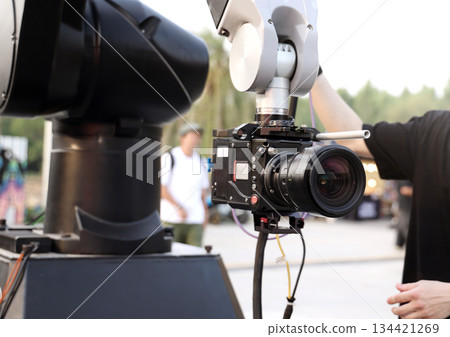 Behind the scenes of movie shooting or video production and film crew team with camera equipment at outdoor location. Video camera with professional robotic arm. BTS of Filming camera setup at outdoor Behind the scenes of movie shooting or video production and film crew team with camera equipment at outdoor location. Video camera with professional robotic arm. BTS of Filming camera setup at outdoor 134421269