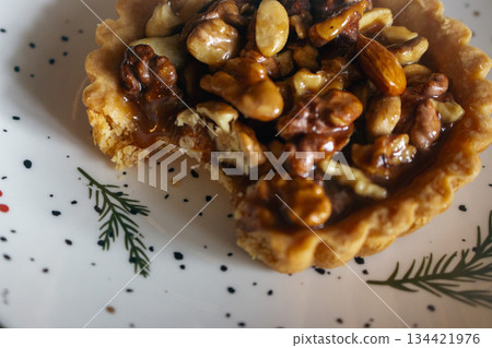 Traditional Christmas tart with nuts and salted caramel on decorated plate. Bitten tart on festive Christmas plate. Bitten hazelnut cake close up. Cinnamon cookie with caramel. Winter holiday food Traditional Christmas tart with nuts and salted caramel on decorated plate. Bitten tart on festive Christmas plate. Bitten hazelnut cake close up. Cinnamon cookie with caramel. Winter holiday food 134421976