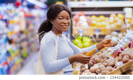 Happy black lady choosing vegetables at grocery store or supermarket, smiling at camera. Millennial African American woman making selection of veggies, purchasing food at mall Happy black lady choosing vegetables at grocery store or supermarket, smiling at camera. Millennial African American woman making selection of veggies, purchasing food at mall 134422080