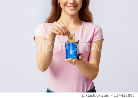 Trash Recycling. Young Woman Putting Card With Paper Waste Icon Into Blue Wooden Toy Garbage Container, Standing Over Light Studio Background, Conceptual Image For Recycle, Copy Space Trash Recycling. Young Woman Putting Card With Paper Waste Icon Into Blue Wooden Toy Garbage Container, Standing Over Light Studio Background, Conceptual Image For Recycle, Copy Space 134422095