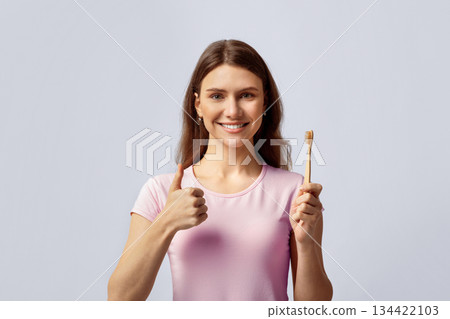 Beautiful Smiling Woman Holding Natural Wooden Bamboo Toothbrush And Showing Thumb Up, Millennial Lady Recommending Eco Products For Dental Care, Standing On Light Studio Background, Copy Space Beautiful Smiling Woman Holding Natural Wooden Bamboo Toothbrush And Showing Thumb Up, Millennial Lady Recommending Eco Products For Dental Care, Standing On Light Studio Background, Copy Space 134422103