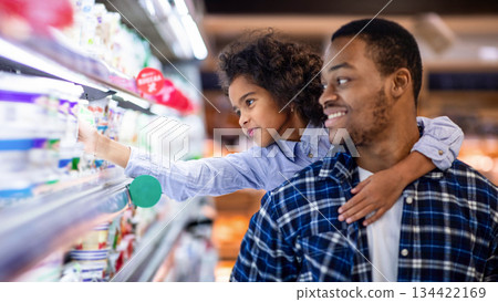 Happy black father with his cute daughter shopping for dairy products at big mall. Lovely girl with her dad purchasing groceries at supermarket, buying foodstuff together Happy black father with his cute daughter shopping for dairy products at big mall. Lovely girl with her dad purchasing groceries at supermarket, buying foodstuff together 134422169