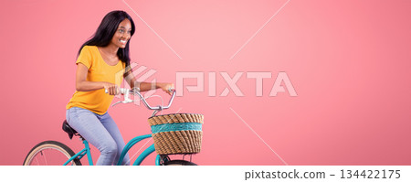 Portrait of pretty African American lady riding vintage bike over pink studio background. Happy black woman on bicycle going for ride. Active lifestyle, tourism and sports concept 134422175
