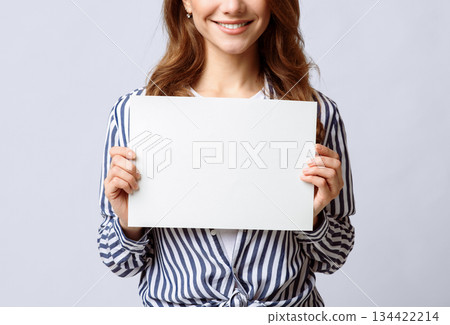 Unrecognizable young lady holding blank sheet of paper in hands, smiling woman demonstrating empty placard with copy space for your text or design, posing over light background, closeup view Unrecognizable young lady holding blank sheet of paper in hands, smiling woman demonstrating empty placard with copy space for your text or design, posing over light background, closeup view 134422214