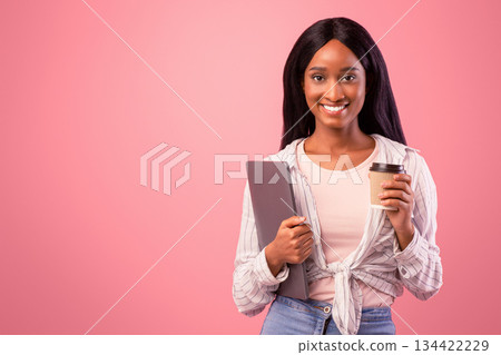 Attractive black lady with laptop computer and takeaway coffee looking at camera on pink studio background. Portrait of African American woman with modern gadget and hot drink posing and smiling Attractive black lady with laptop computer and takeaway coffee looking at camera on pink studio background. Portrait of African American woman with modern gadget and hot drink posing and smiling 134422229